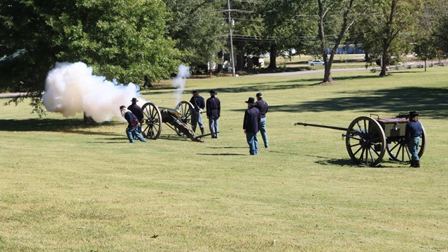 Smoke belches from a cannon as living historians present a demonstration. 