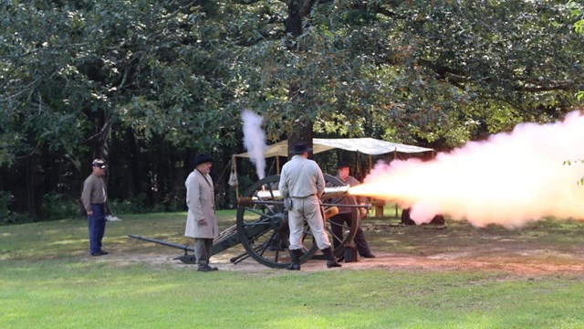 Living historians in period uniforms fire a bronze cannon. 