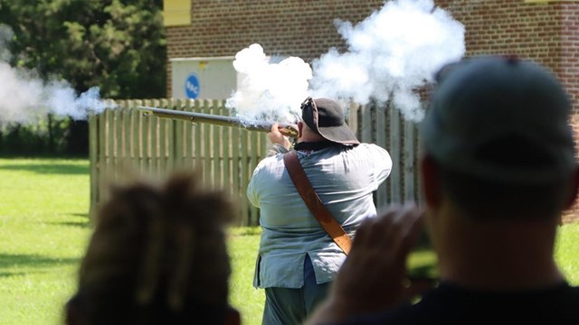 Living historian in uniform fires a musket. 