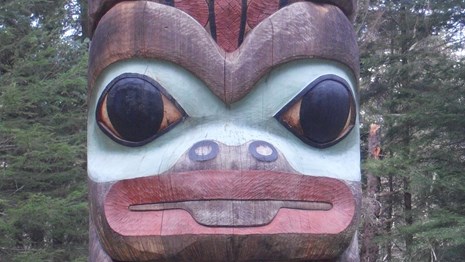 Close up photo of a formline frog and raven at the base of the K'alyaan Totem Pole.