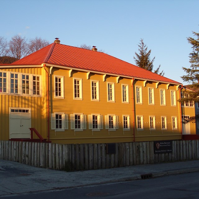 sun shining on a large two story rectangular yellow building with a res roof and multiple windows 