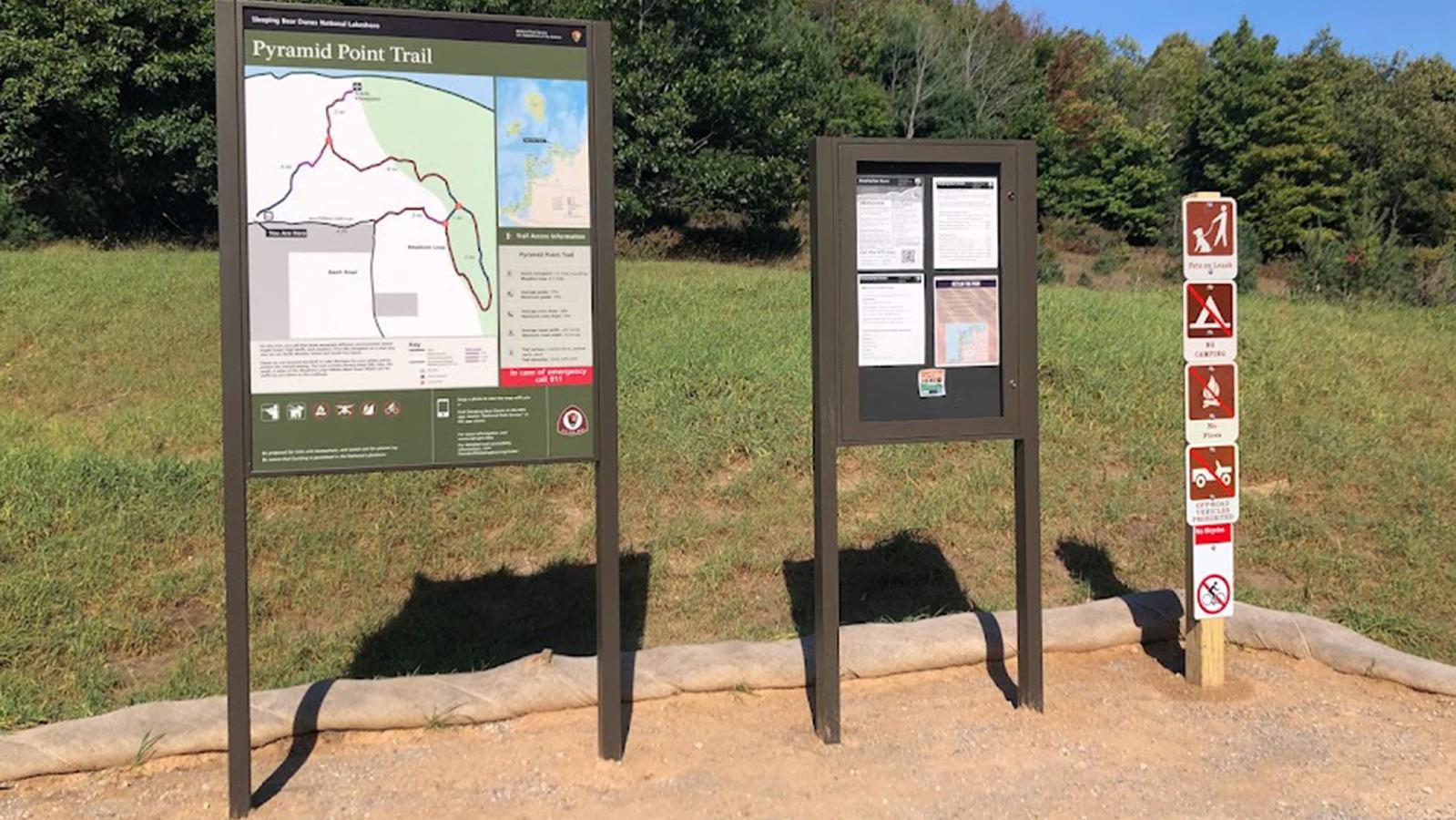 An upright trailhead panel next to a bulletin board and regulation signs.