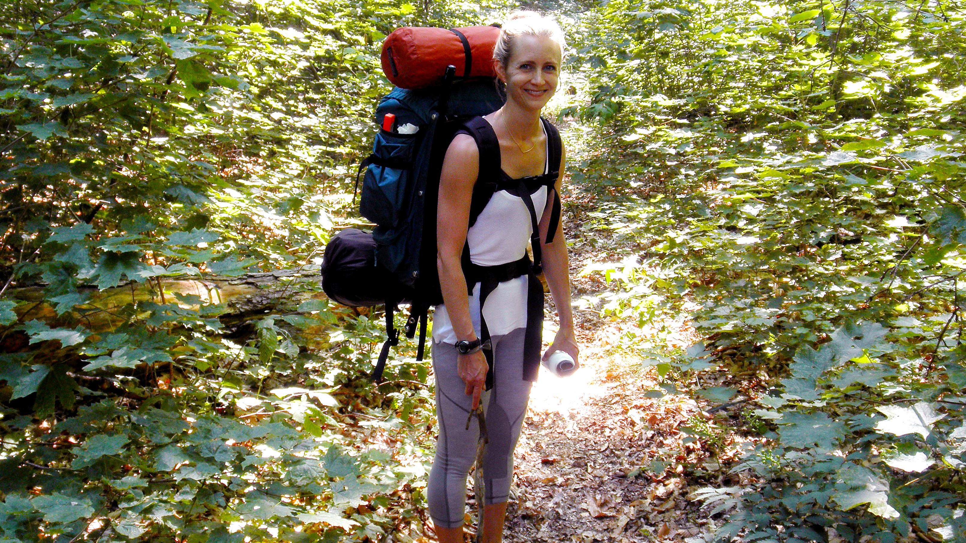 A young woman with backpack smiles on the hiking trail