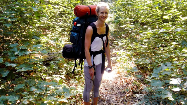 A young woman with backpack smiles on the hiking trail