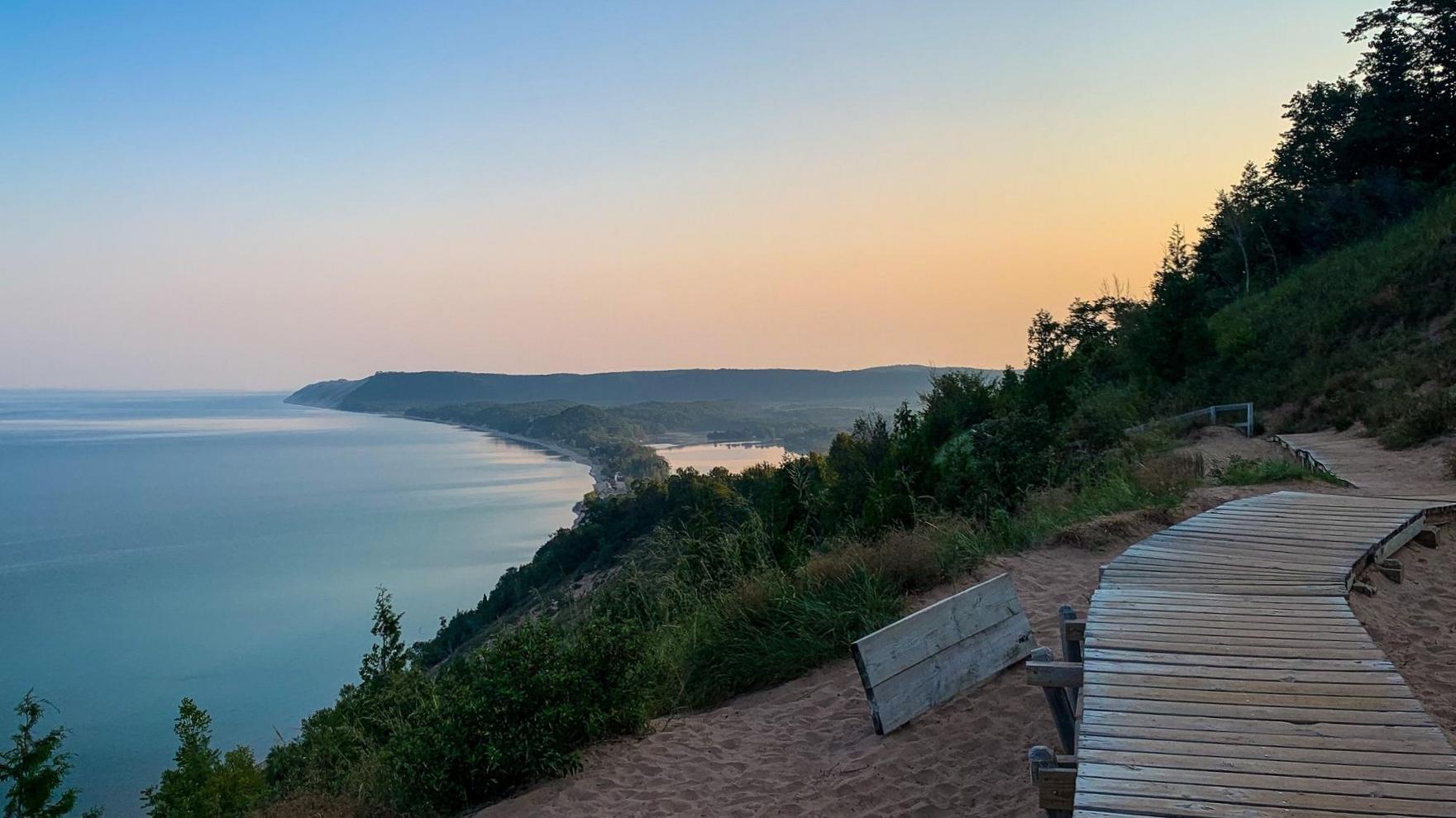 From the top of the bluff, looking back - a hazy, colorful sunrise amongst a blue lake and trees. 