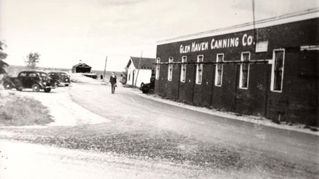 Historic photo of the cannery building with 1940-era cars parked behind.