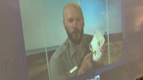 Ranger on a tv screen holds up a skull during a distance learning program
