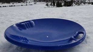 A blue sled sits atop a snow-covered dune.