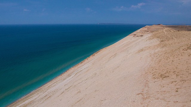 A steep rocky sand dune with a large body of water beyond