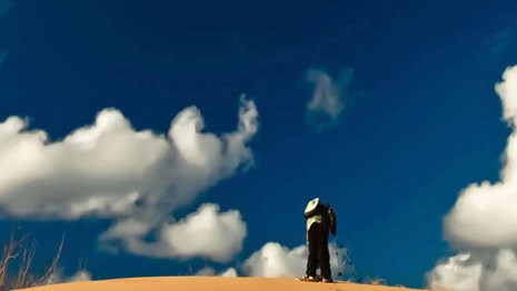 Man stands on top of dune with blue sky and white clouds above