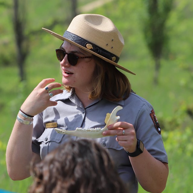 A ranger holds the jawbone of a tree while pointing to her own jaw.