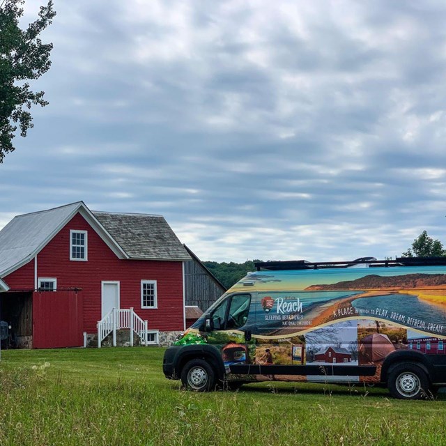 A colorful van next to a red farm.