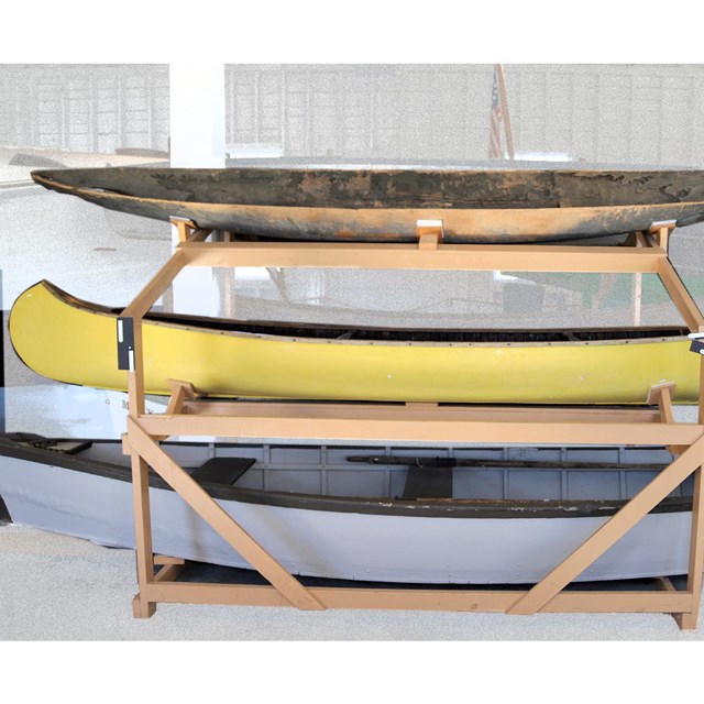 A rack holds three boats: a dugout canoe, a yellow canoe, and rowboat