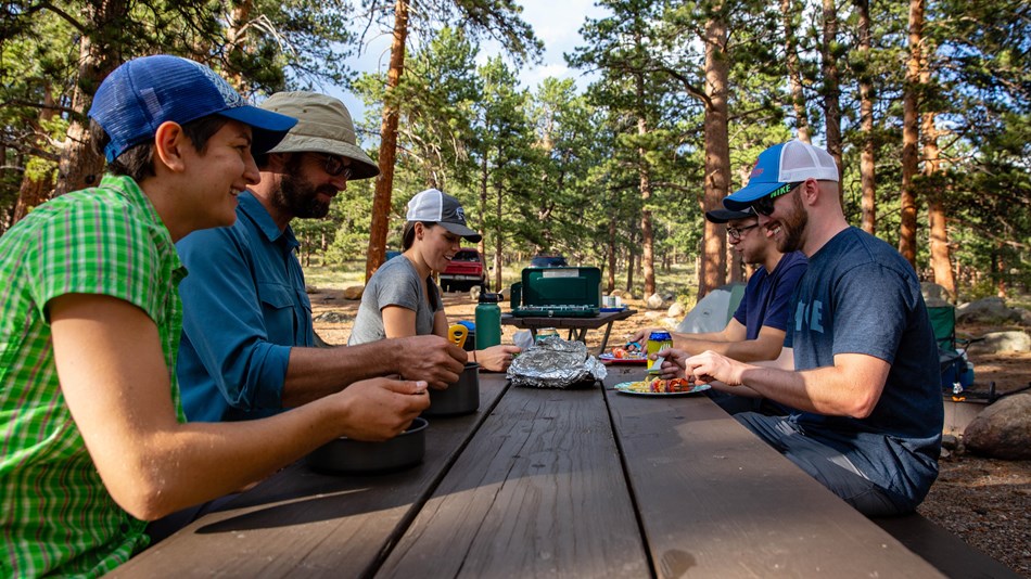 Visitors eat a meal at a picnic table at a campground in Rocky Mountain National Park.