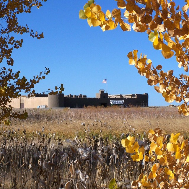 Bent's Old Fort viewed from afar, through yellow fall leaves and across open grassland