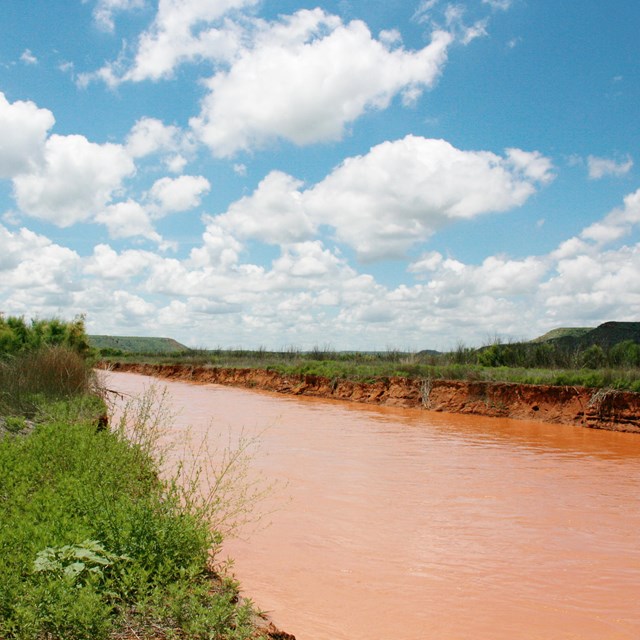 Red water of the Canadian River cutting through a green landscape