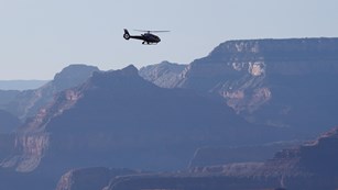 A helicopter flies past rugged canyon walls at Grand Canyon National Park.