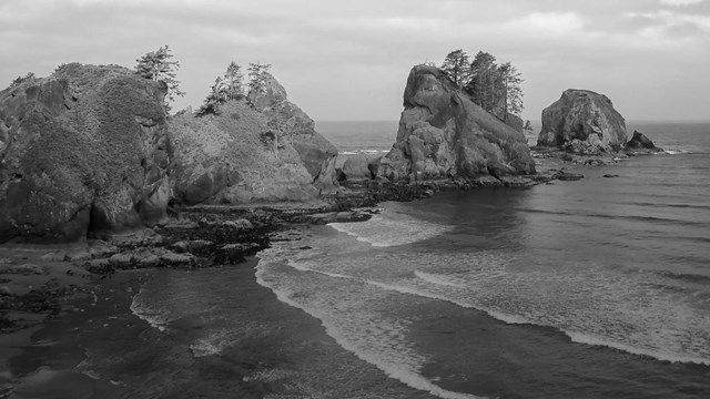 Black-and-white photo of impressive rocky stacks rising up above an expansive coastline.