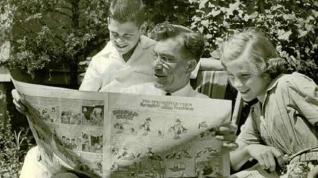Man and children gather around a newspaper.