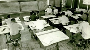 A black and white photo of men sitting at drafting desks at an apprentice school. 