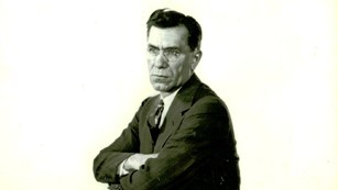 A black and white photo of a man sitting backwards on a chair. 