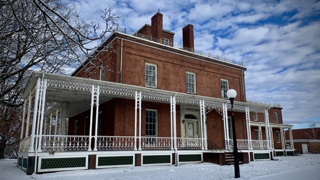 A multistory red building with a covered porch and copula during winter on a bright day.