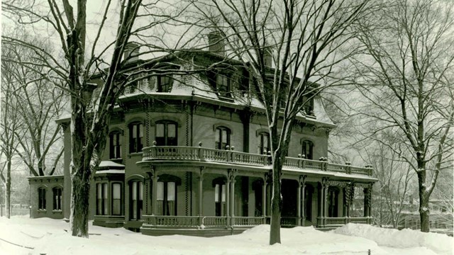 A black and white photo of a multistory building behind trees on a winter day. 