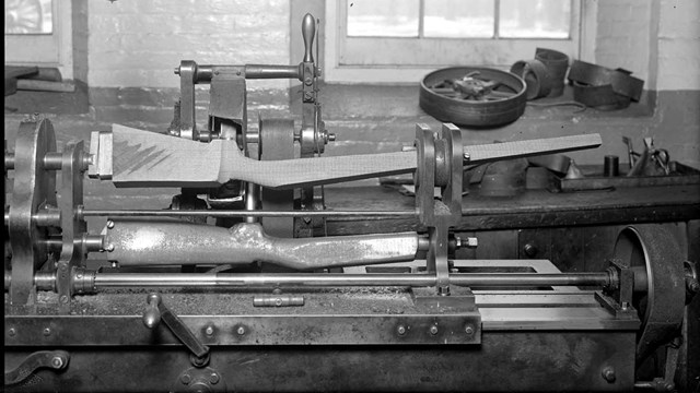 A black and white photo of o a modern lathe trimming a gunstock. 