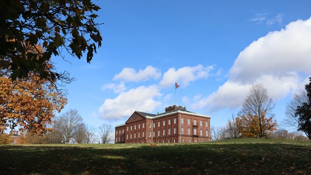 A building sitting on a hill with a flap on top. The building is framed in by trees. 