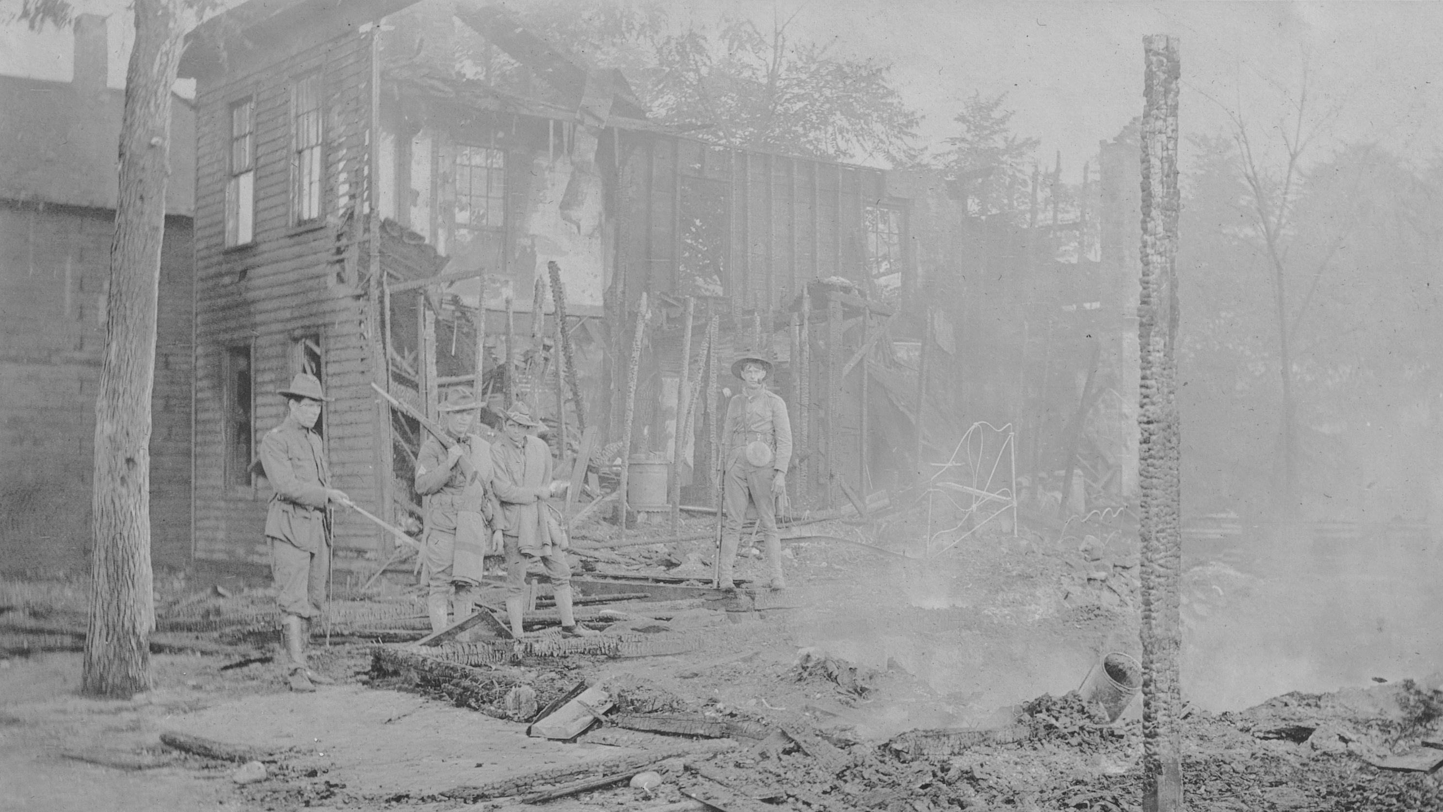 Historic photo of soldiers standing in the burned remains of a building.  