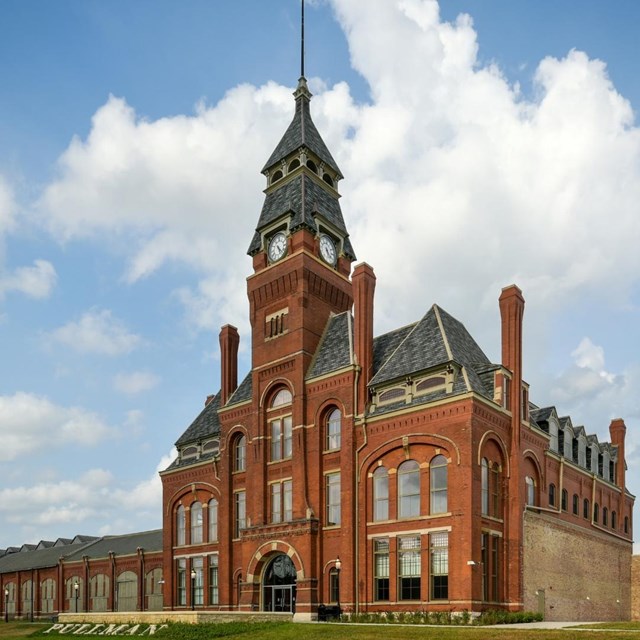 A large, red brick clock tower with a tall, black pointed roof.