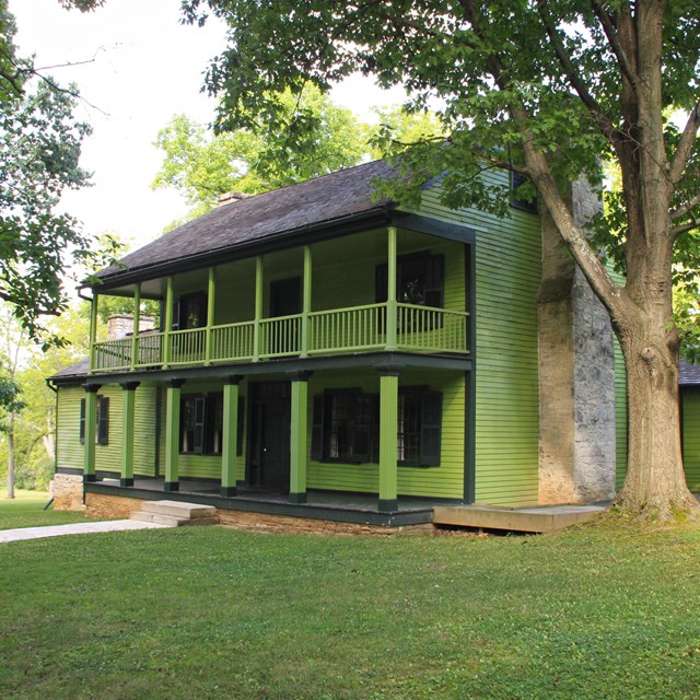 A two-story house with lime green siding and a gray roof, surrounded by grass and trees.