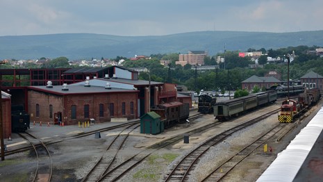 View of railyard taken from elevated walkway. View of city and mountains in the background.
