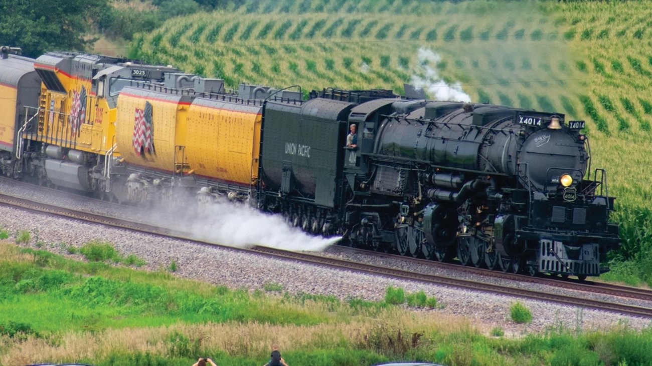Large steam locomotive steaming through farm fields
