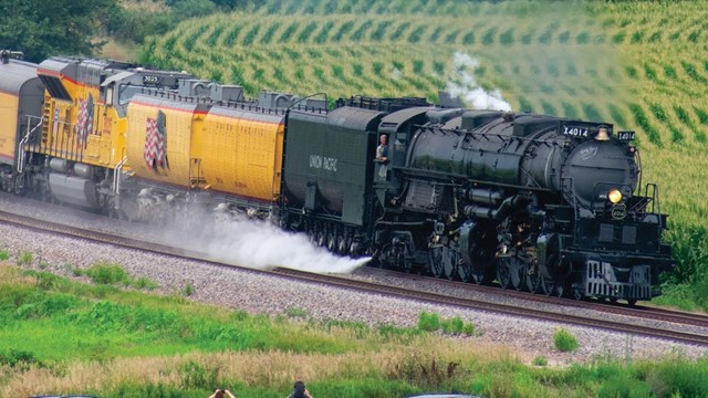 Large steam locomotive steaming through farm fields