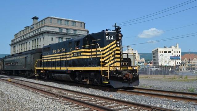 Diesel Engine pulling passenger coaches past the Radisson Lackawanna Station