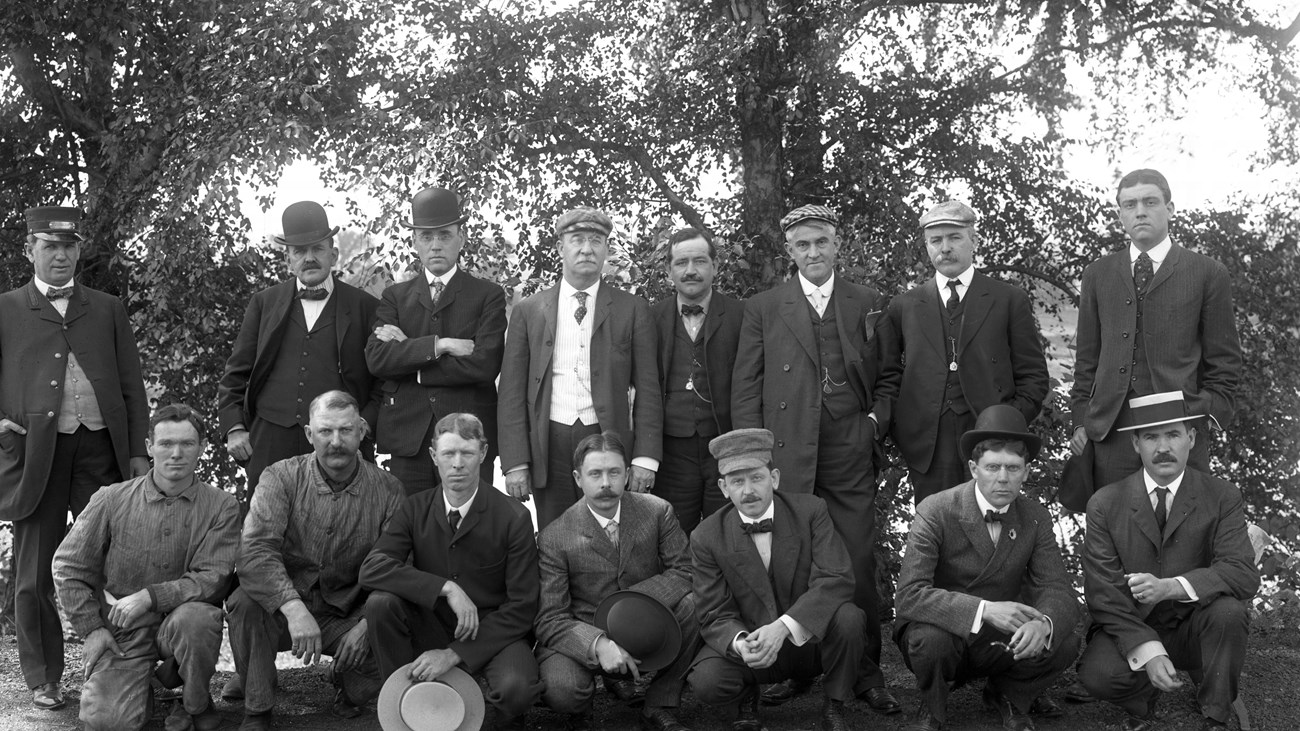 Men in 1920s business attire standing in a group with a wooded backdrop