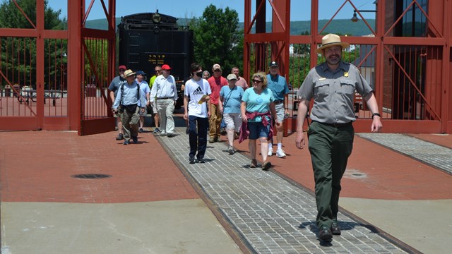 A park ranger leads a group of 15 people through a tall iron gate