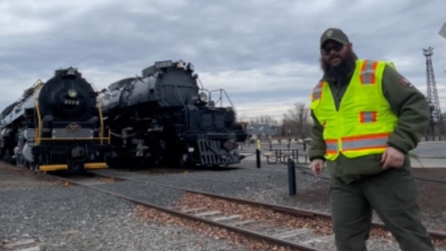 A ranger stands on the boardwak with two locomotives in the background