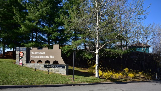 an entrance sign in the shape of a train, surrounded by budding trees and flowers