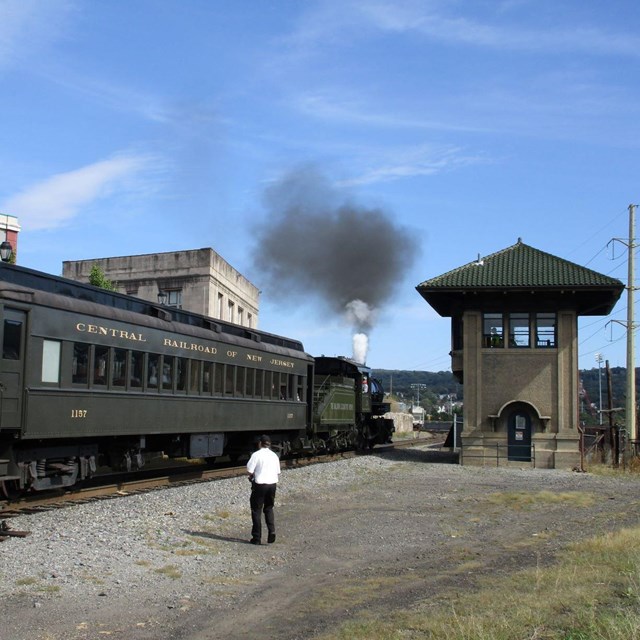 A passenger train on the track with a lone onlooker safely in the distance