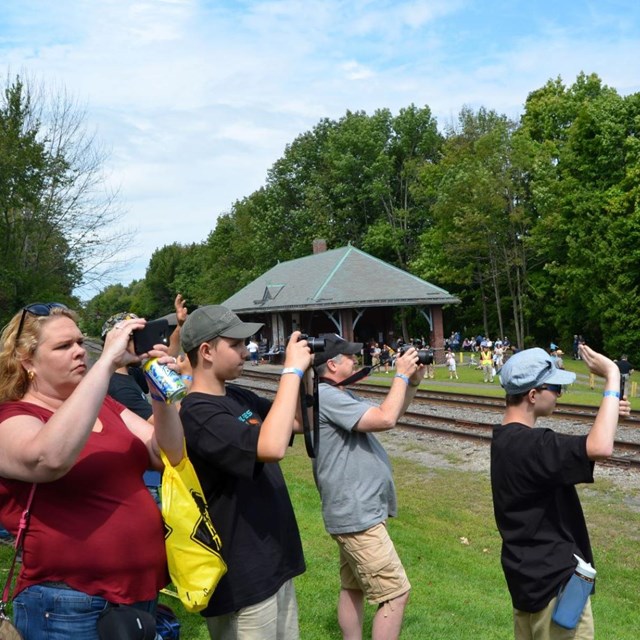 A group of visitors standing safely away from tracks and holding cameras in the air for photos