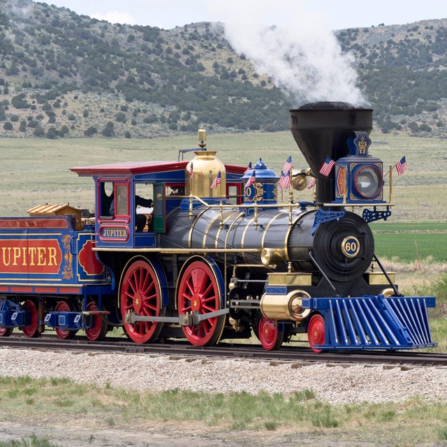 vibrant colored steam engine moving on track with a field and mountains in the distance