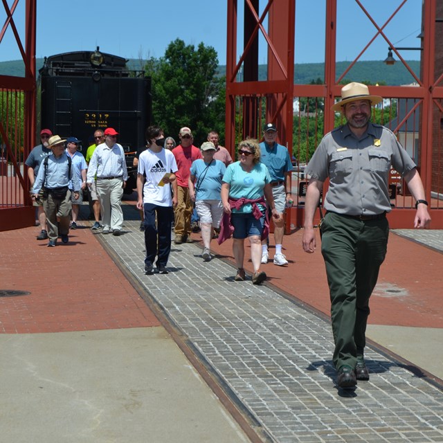 A park ranger leads a group of 15 people through a tall iron gate