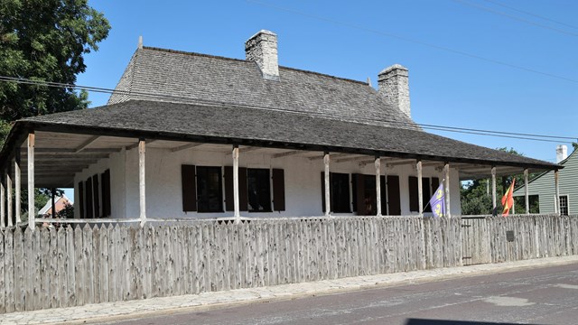 Home with rap around porch and a palisaded fence. 