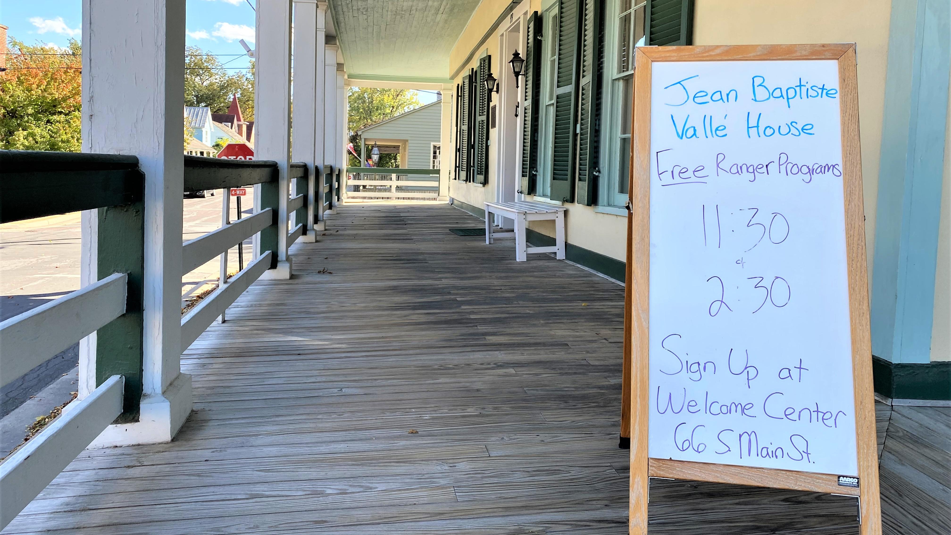 Whiteboard sign with tour times sitting on a covered porch. 