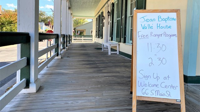 Whiteboard sign with tour times sitting on a covered porch. 