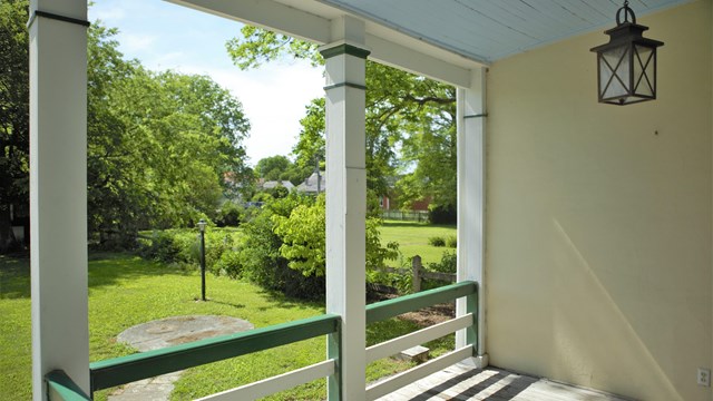A light fixture hangs above a porch with green railings and white posts. 