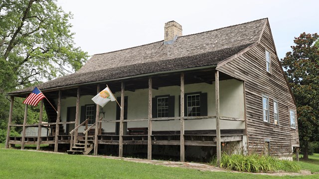 Wooden house with a white wall under a covered front porch. 