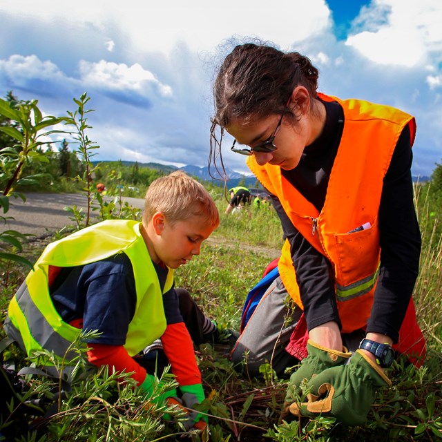 a young boy and girl in safety vests pull weeds